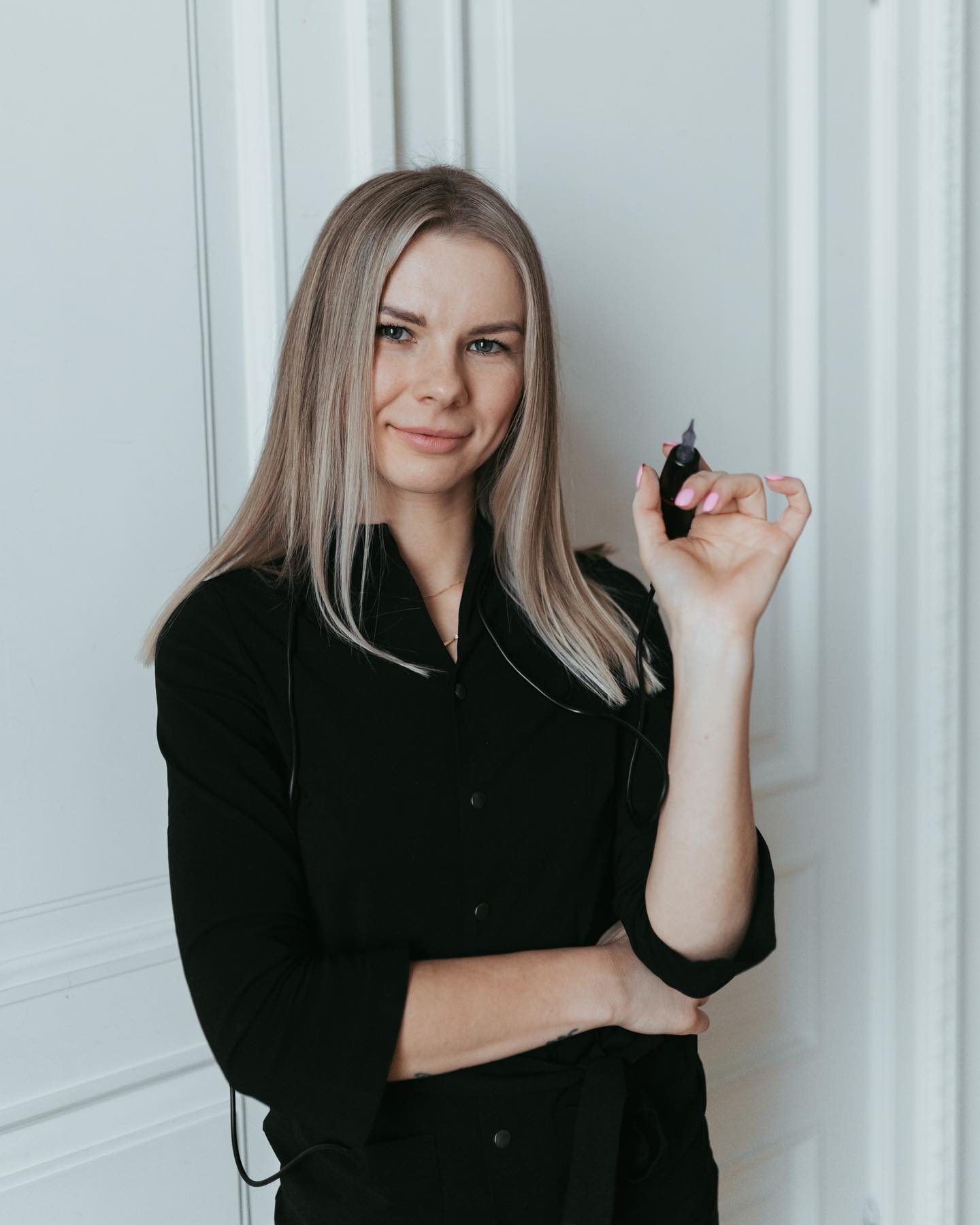 In the image, Yulia, the founder of Natural Brows Bar, is holding a brow tattooing device with a poised expression, indicative of professional expertise in the beauty industry. Her attire suggests a blend of professional and approachable style, suitable for a specialist in a client-facing role.