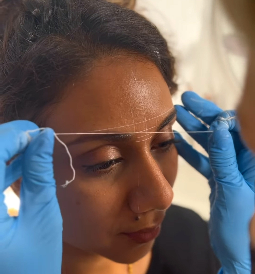 The image shows the process of brow mapping, which is a key step in designing the shape for powder brows. Brow mapping involves using a thread or tool to outline the desired shape of the eyebrows before the application of semi-permanent makeup, ensuring symmetry and precision in the final look. This technique is crucial for achieving the most flattering brow shape for the individual's facial features.